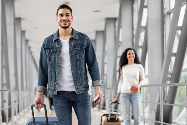 smiling middle eastern man and woman walking with luggage at airport