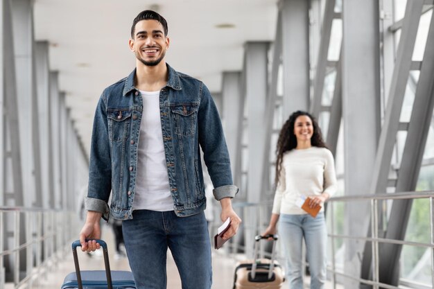 Smiling middle eastern man and woman walking with luggage at airport