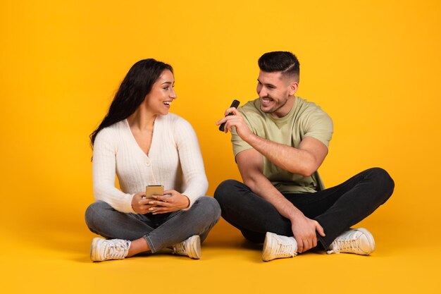 Smiling millennial arabic male showing smartphone to amazed wife recommending app sit on floor