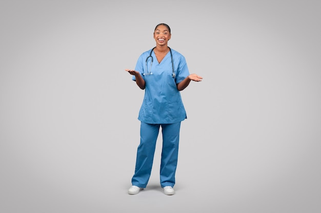 Photo smiling millennial black doctor surgeon nurse in blue uniform hold copy space on hands spread hands