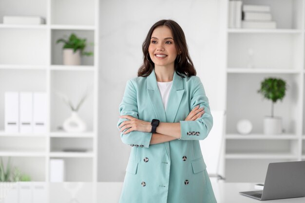 Smiling millennial caucasian lady in suit with crossed arms looks at empty space