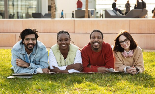 Photo smiling millennial diverse modern students study together rest from lesson lie on grass in