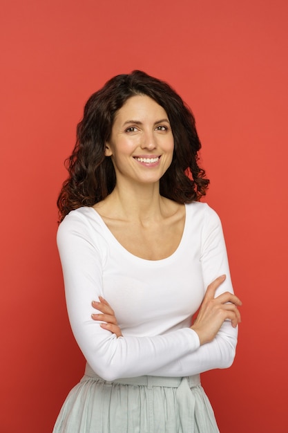 Smiling millennial woman with crossed hands look in camera dressed in white with natural curly hair