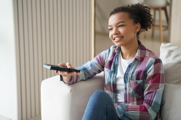 Smiling mixed race girl changes TV channel with remote control watching television series on sofa