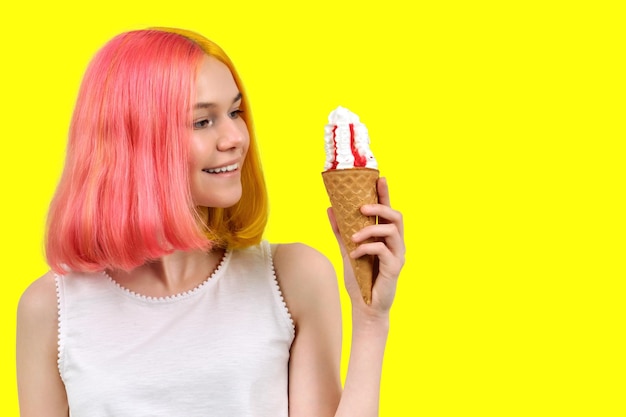 Smiling model teenager with ice cream in waffle cone over yellow background