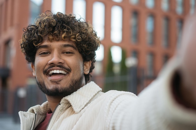 Foto sorridente uomo indiano moderno che prende selfie, fa una videochiamata per strada. concetto di tecnologia moderna