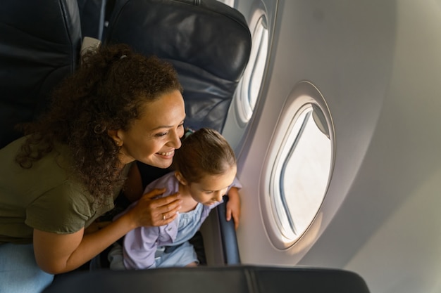 Smiling mom and her kid looking at the scenery outside the plane window