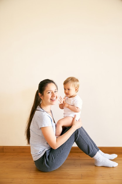 Smiling mom sitting on the floor and holding a small baby on her lap