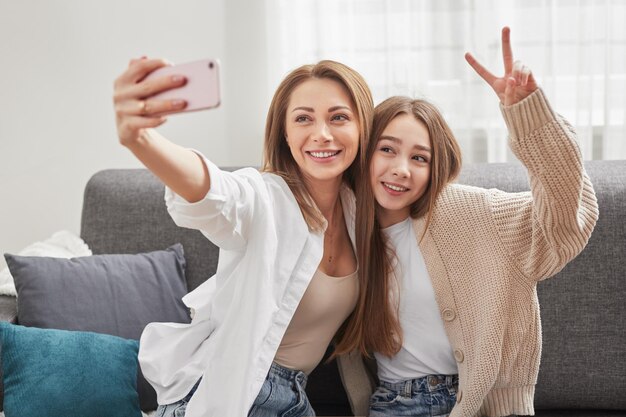 Фото Улыбающиеся мать и дочь делают селфи на смартфоне на диване