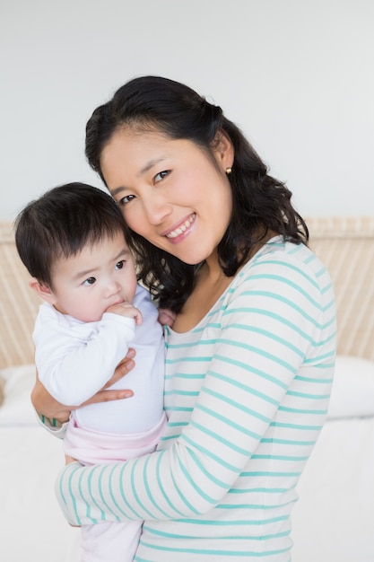 Smiling mother carrying baby daughter in bedroom