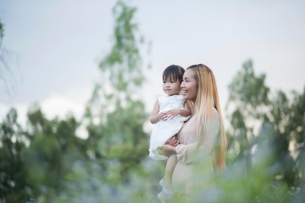 写真 笑顔の母親が植物の真ん中に立って娘を抱いている