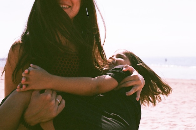 smiling mother carrying daughter while standing at beach