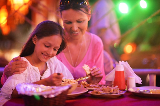 Smiling mother and daughter eating in cafe in evening