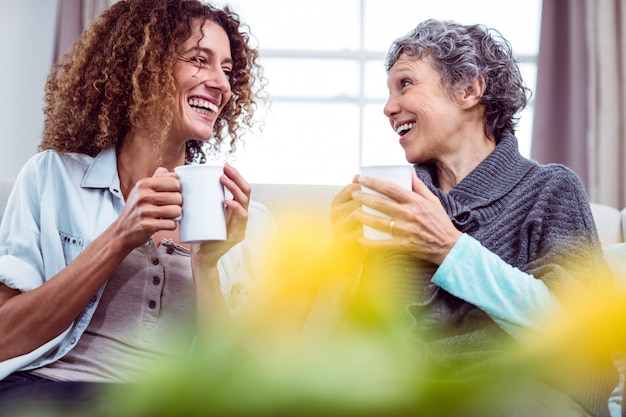 Photo smiling mother and daughter holding coffee mugs while discussing