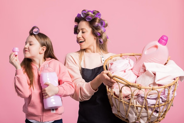 웃고 있는 엄마와 딸이 빨래 바구니를 들고 분홍색 배경에 포즈를 취하고 있다