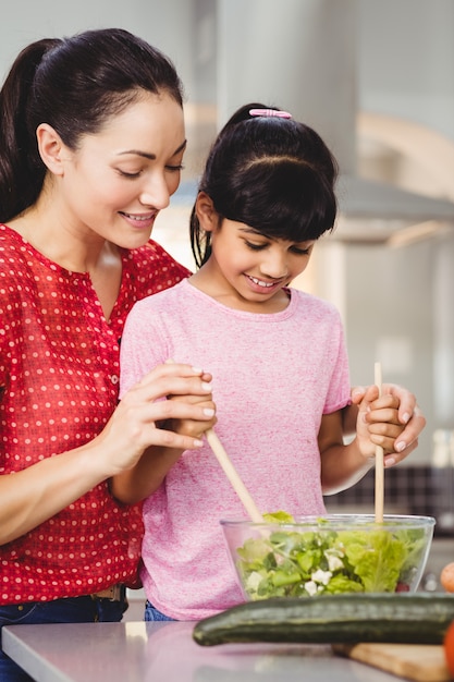 Smiling mother and daughter preparing salad