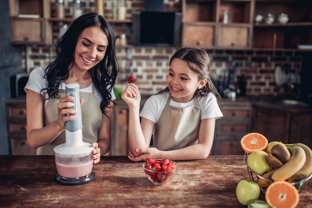 Smiling mother and daughter preparing smoothie using blender on the kitchen