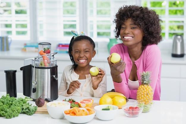 Smiling mother and daughter preparing strawberry smoothie in kitchen at home