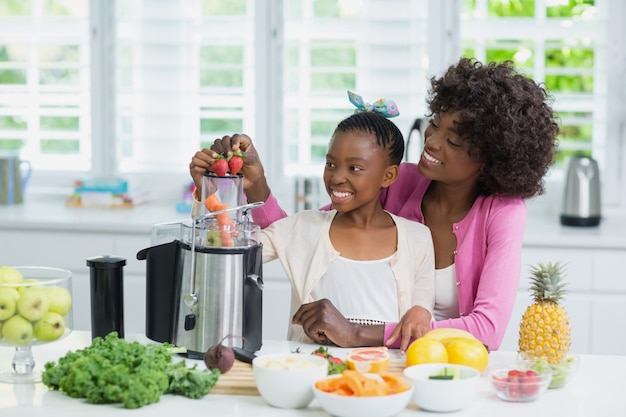 Madre e figlia sorridenti che preparano il frullato della fragola in cucina