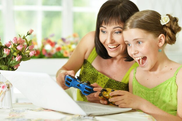 Smiling mother and daughter sitting at table and playing computer game on laptop