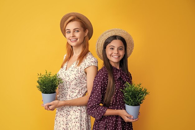黄色の背景に鉢植えの植物を持つ母と娘の笑顔