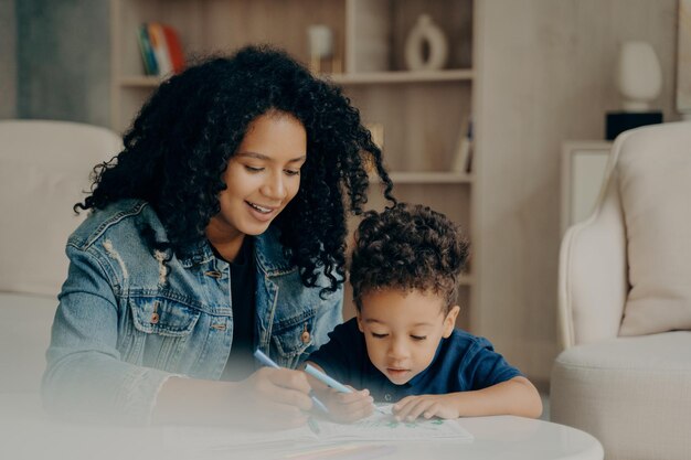 Photo smiling mother drawing with son in book