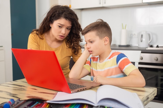 Улыбающаяся мать помогает очаровательному сыну делать домашнее задание дома