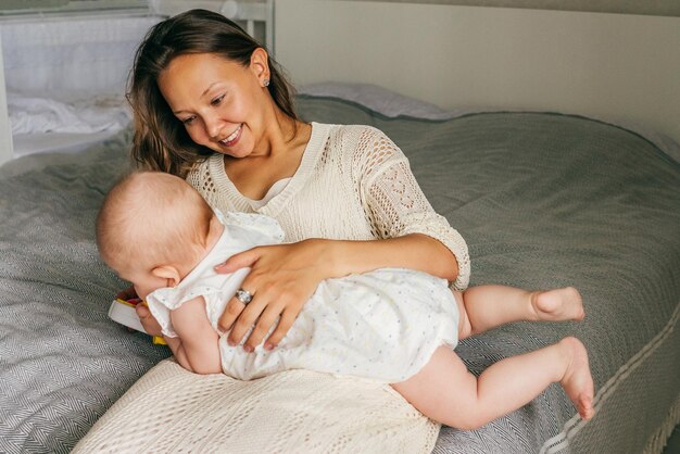 Photo smiling mother holding baby girl while lying on bed