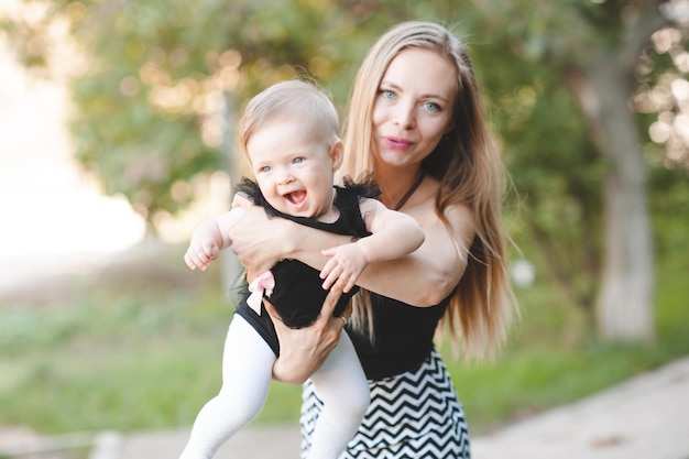 Smiling mother holding happy cheerful baby girl playing outdoor in park over nature