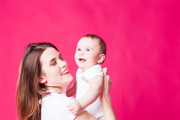 Улыбающаяся мать держит своего смеющегося ребенка, изолированного на розовом фоне