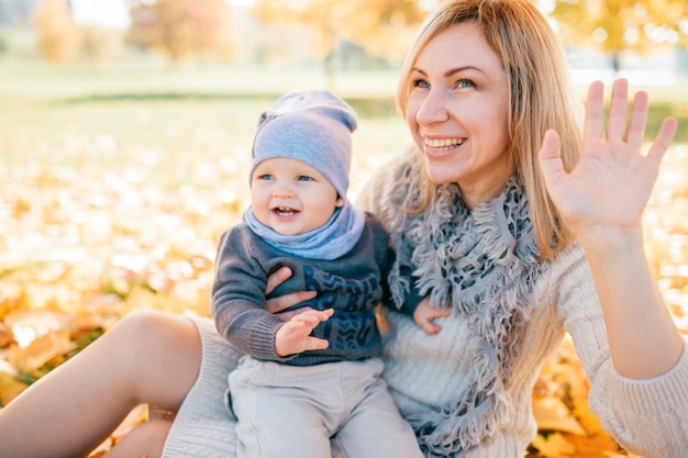 Smiling mother holding her lovely son on her knees in autumn park