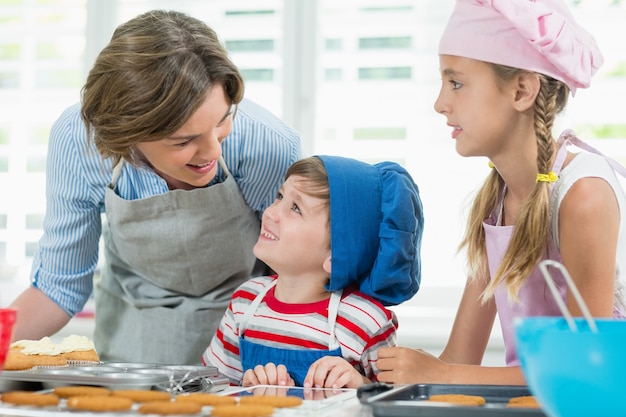 Улыбающаяся мать и дети общаются друг с другом во время приготовления печенья