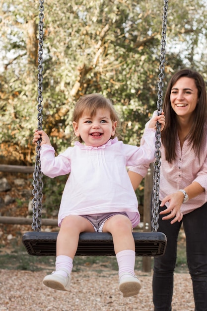 smiling mother looking at daughter while swinging in playground