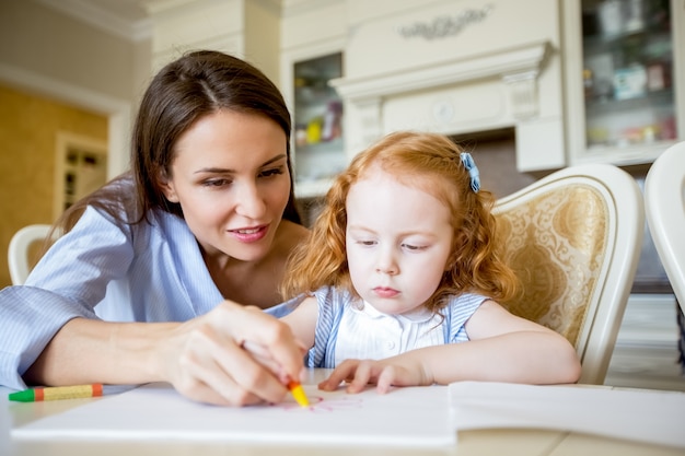 Smiling mother or nanny drawing with little girl