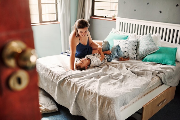 Smiling mother playing with son lying on bed at home