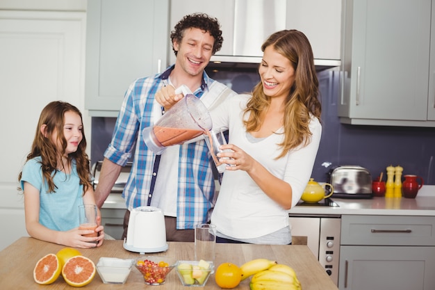 Succo di frutta di versamento sorridente della madre in un vetro con la famiglia