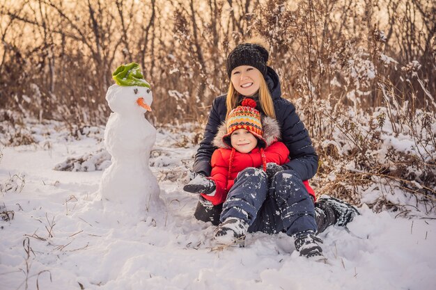 Smiling mother and son making a snowman outdoor