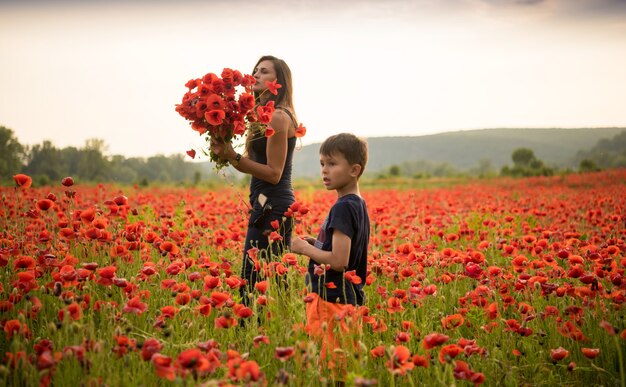 Sorridente madre e figlio in posa sul campo di papaveri al tramonto