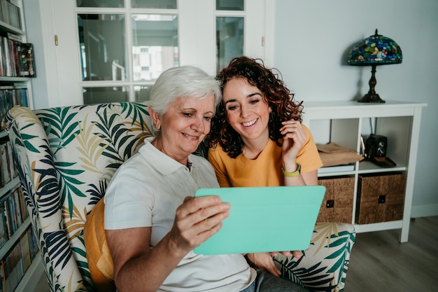 Photo smiling mother watching video with daughter over digital tablet at home