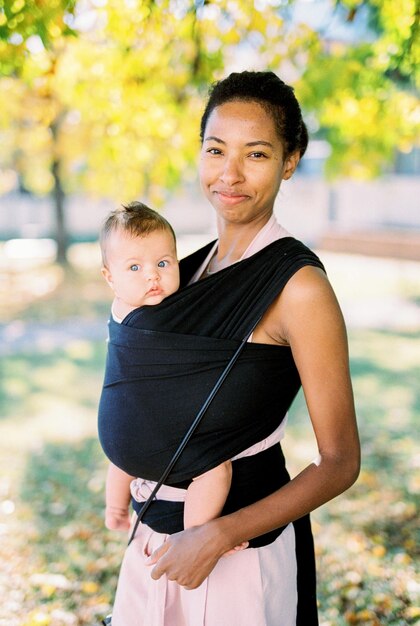 Photo smiling mother with baby in sling in park