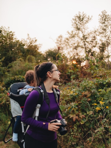 Foto madre sorridente con figlio carino sulla schiena in piedi sulla foresta