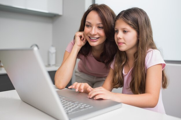 Smiling mother with daughter using laptop in kitchen