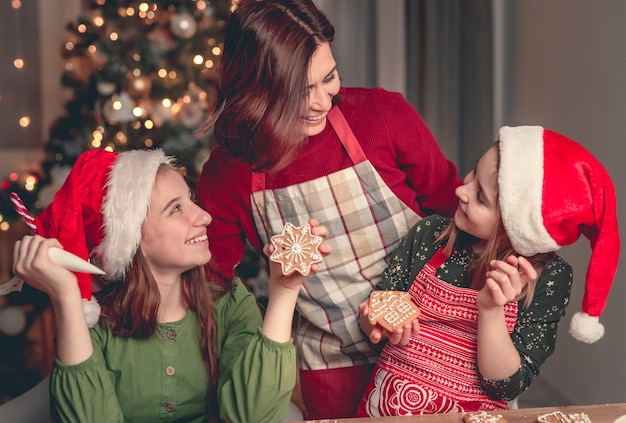 写真 自宅でクリスマスツリーの近くでジンジャーブレッドを焼く娘と笑顔の母