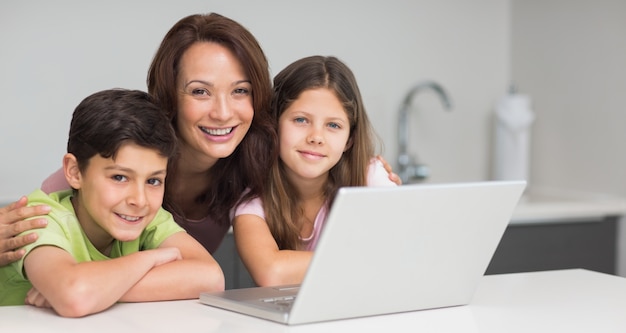 Smiling mother with kids using laptop in kitchen