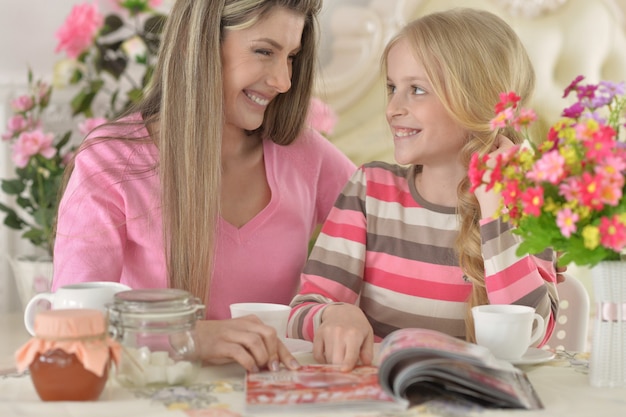 Smiling mother with little daughter drinking  tea with magazine at kitchen