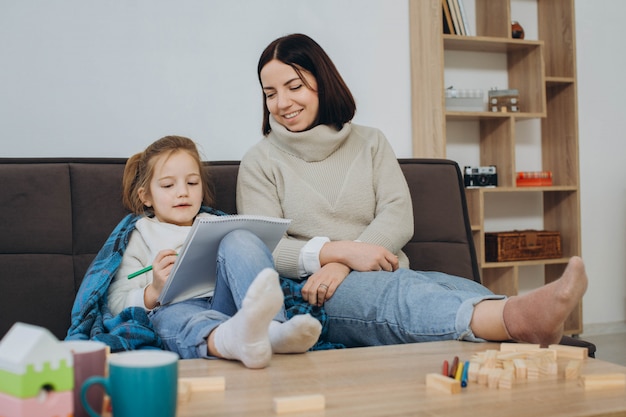 Smiling mother with preschool daughter drawing with colored pencils