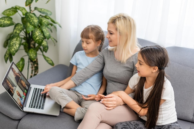 Smiling mother with young kids using laptop at home.