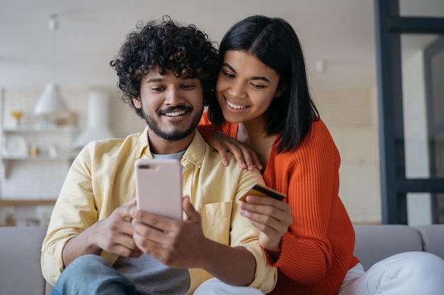 Smiling multiracial couple holding credit card shopping online ordering food sitting at home