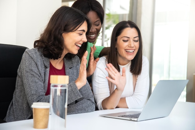 Smiling multiracial coworker women wave hello during business video call using laptop Business and technology concept