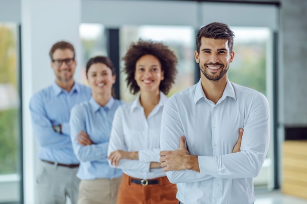 Smiling multiracial group of business people standing with arms crossed and looking at camera while standing in office. Selective focus on man in foreground.